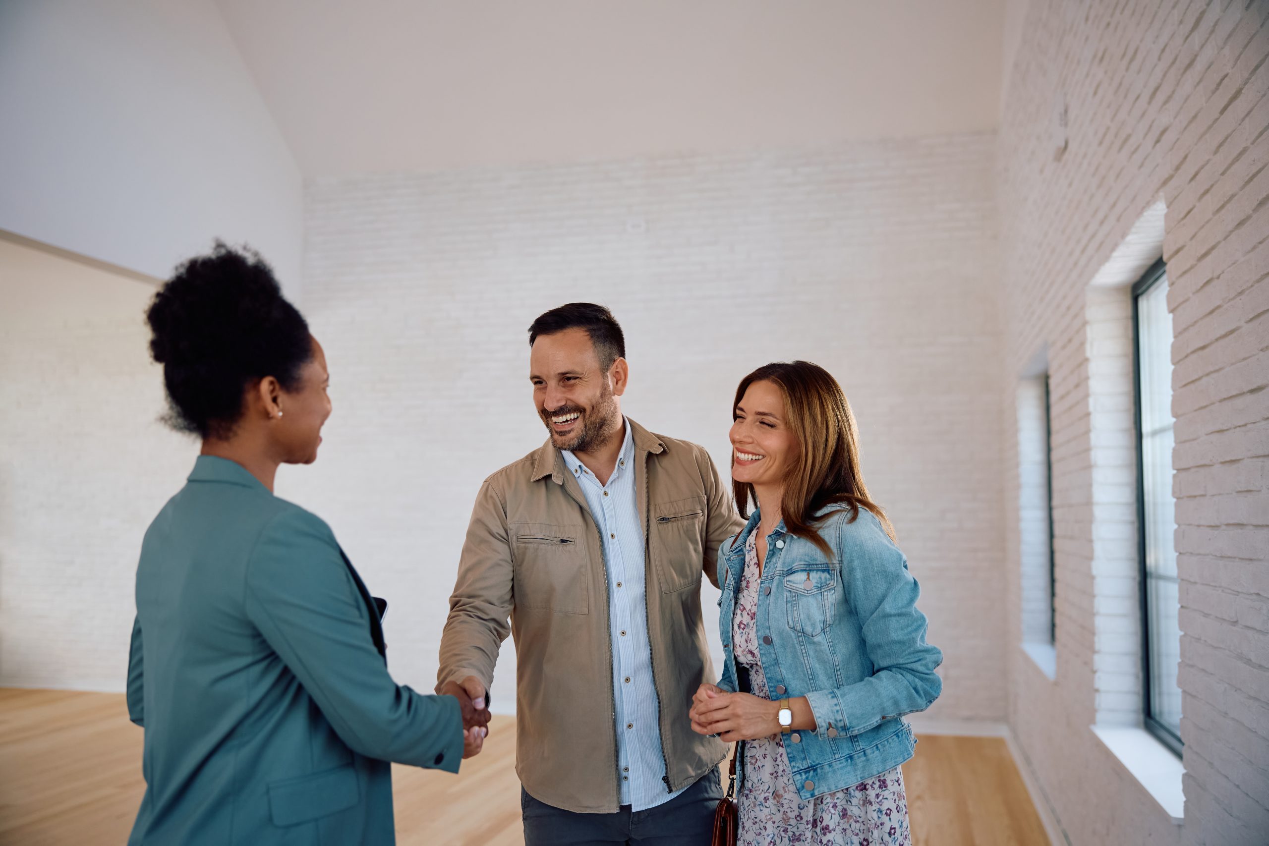 Happy real estate buyers shaking hands with African American female agent during open house day.